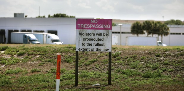 An old No Trespassing sign on the north side of the site of the former Siemens-Stromberg telecommunications plant that closed in 2003, photographed Tuesday, April 11, 2023. In the background, trucks from a shipping business in the repurposed facility. The Siemens-Stromberg complex was located at 400 Rinehart Road in Lake Mary and was designated a hazardous waste site after groundwater contamination from solvent use in manufacturing was discovered in numerous onsite environmental tests over the last 20 years. (Joe Burbank/Orlando Sentinel)